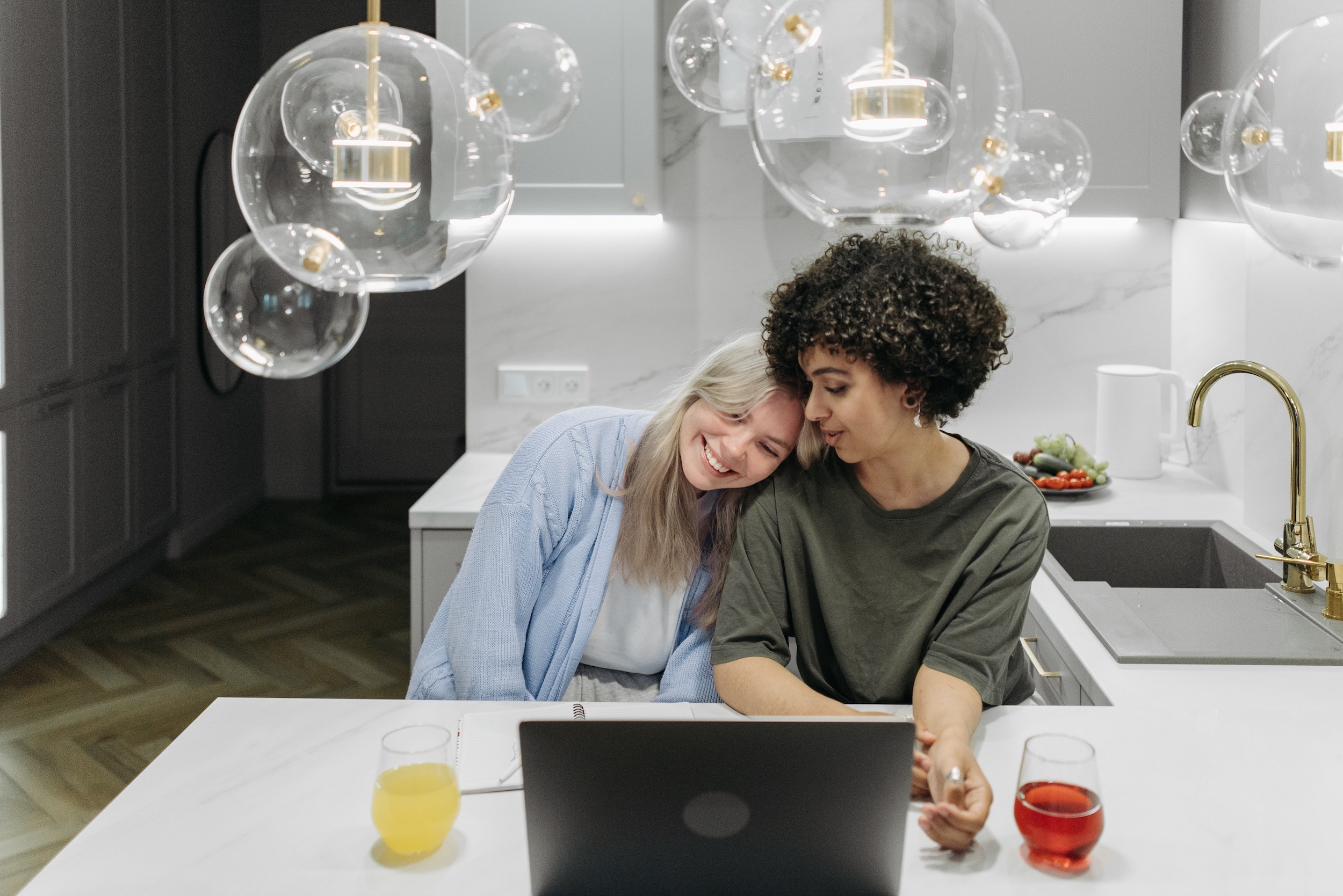 Two women at a laptop, one rests her head on the other's shoulder
