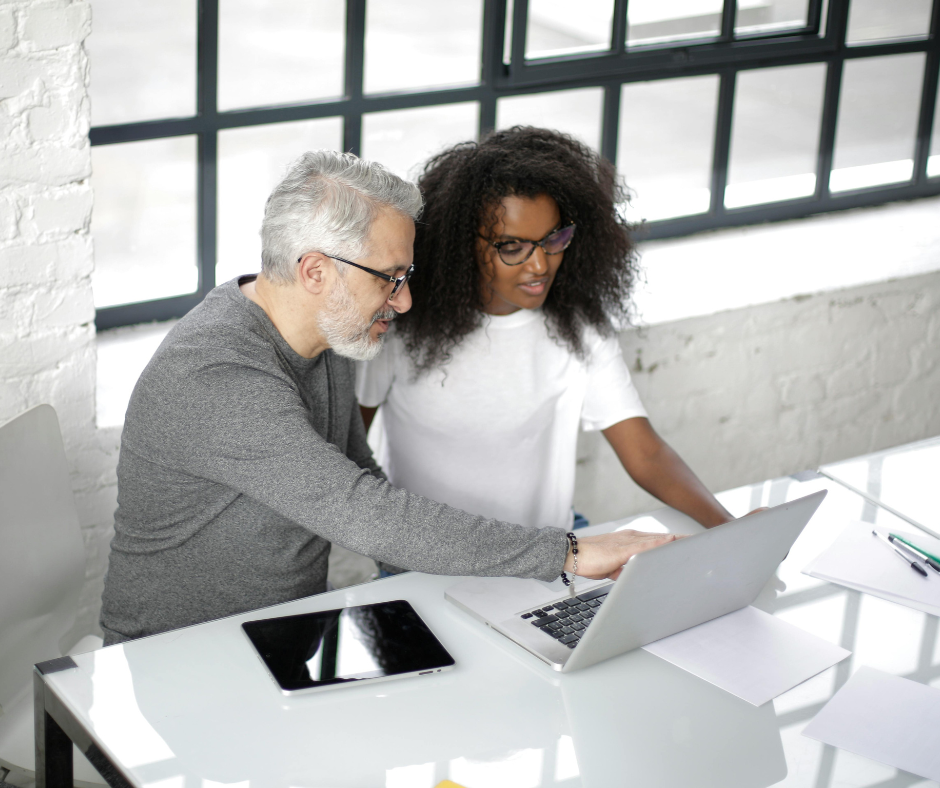 man and woman sit at table conversing and looking at a laptop