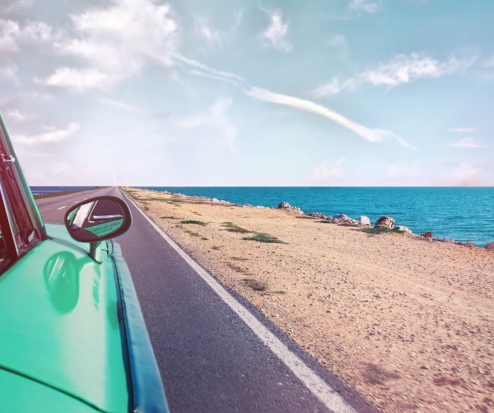 a vintage car driving along a coastal road