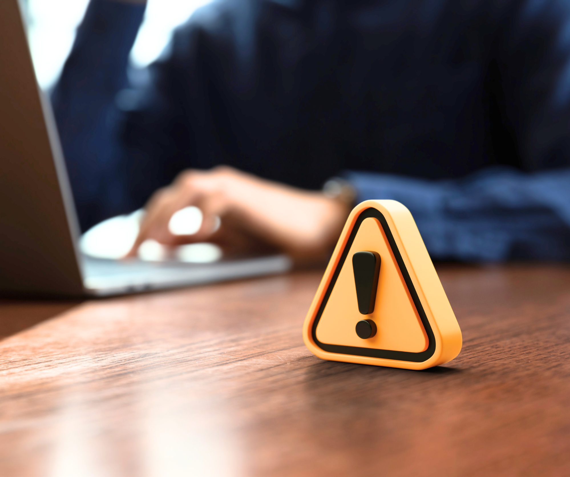 person typing at laptop with a warning sign on the table next to them