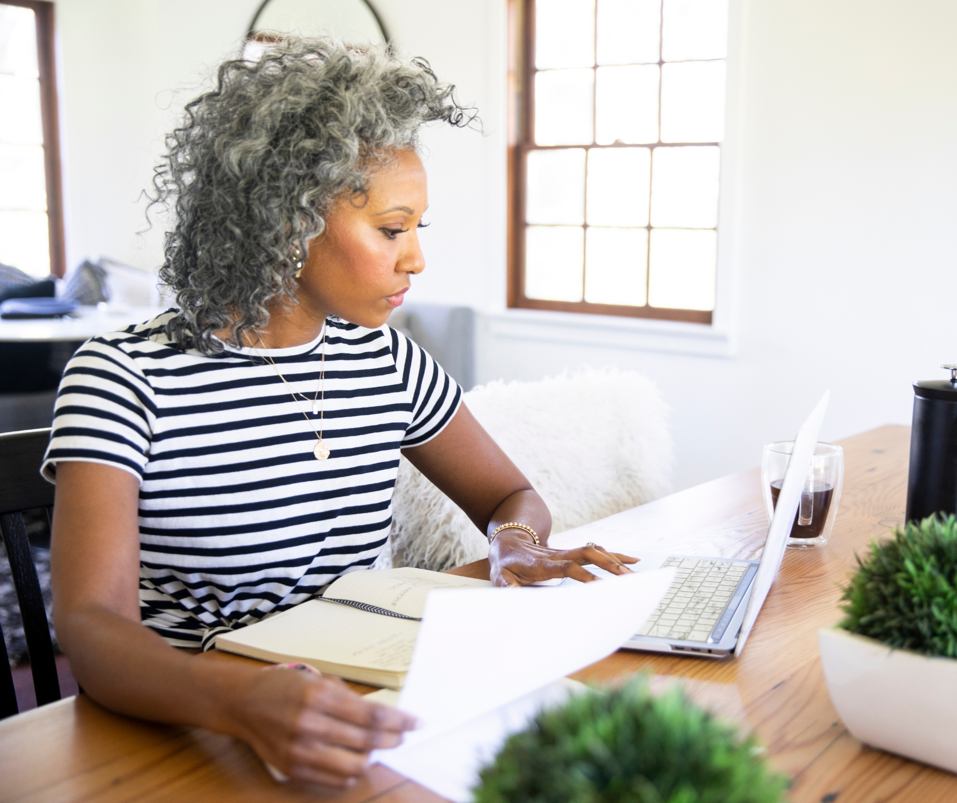 woman sat at table, looking at laptop and papers with a concerned expression